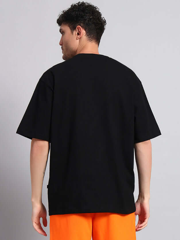 Back view of a model wearing HULK OVER-SIZED T-SHIRT BLACK MEN paired with orange shorts, displaying summer fashion.