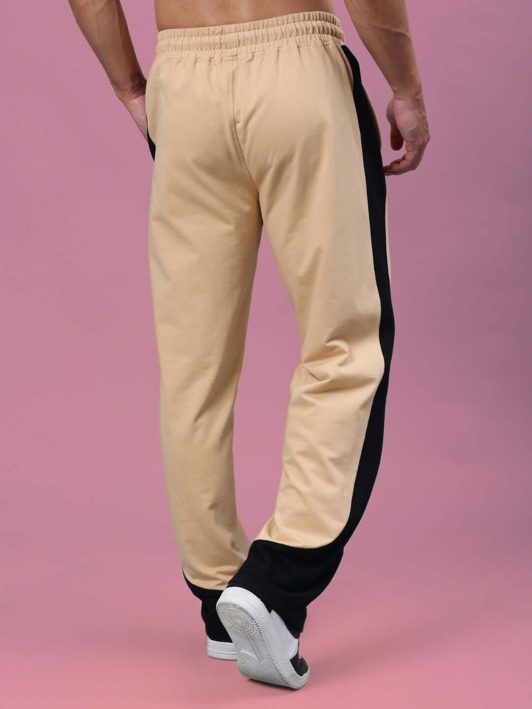 Rear view of beige-black HURTLE Baggy Joggers by DUDS, showcased on a male model against a pink backdrop.