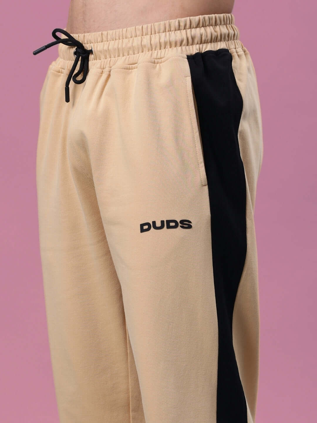 Beige and Black Hurtle Baggy Joggers by DUDS with adjustable drawstring on pink background.