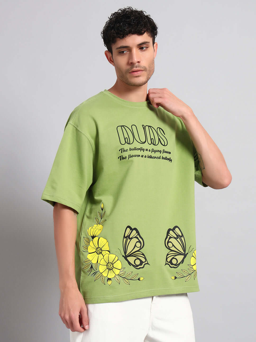 Man wearing IKON BUTTERFLY T-SHIRT GREEN MEN with striking butterfly graphic and yellow flowers, showcasing fashion-forward streetwear style.