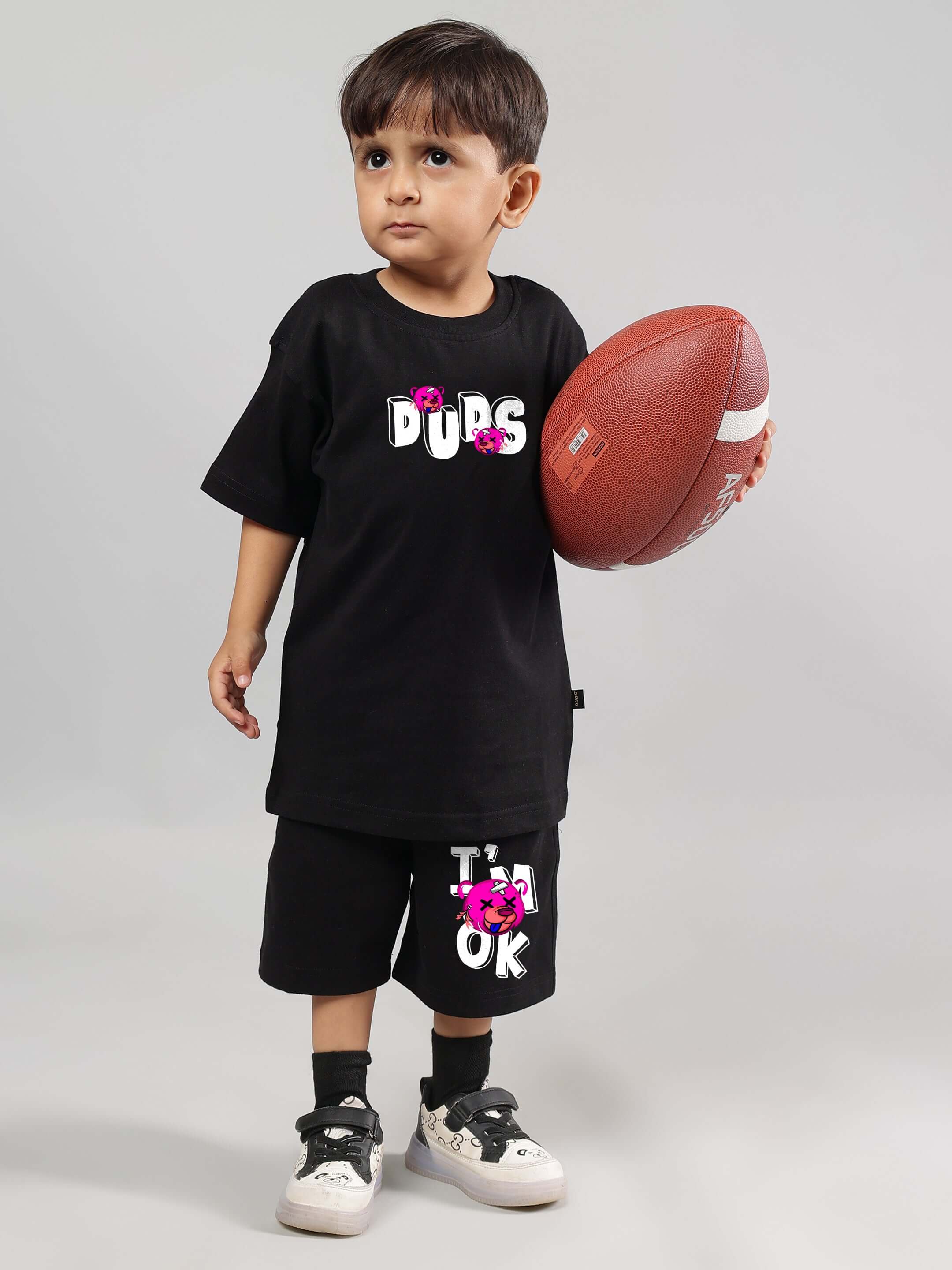 Toddler wearing black I'M OK co-ord set by DUDS, holding a football. Fashion for boys and girls, customizable fit available.