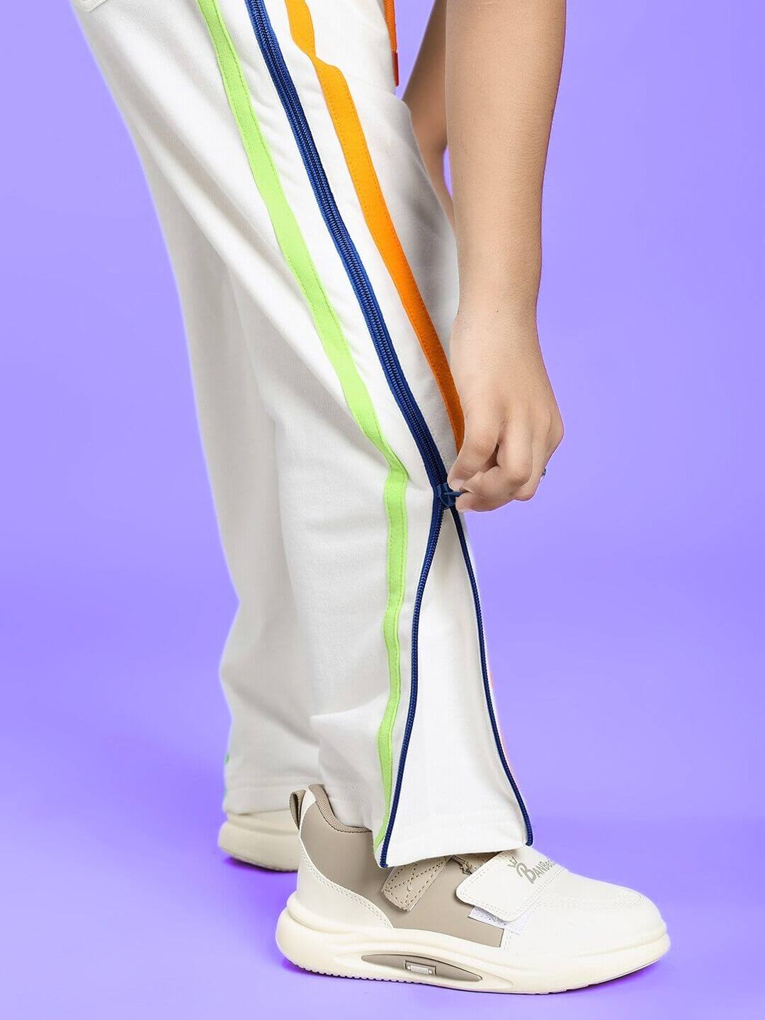 Child wearing IMPERIAL SIDE ZIPPER JOGGER FOR BOYS AND GIRLS OFF WHITE with colorful side stripes, adjusting zipper.