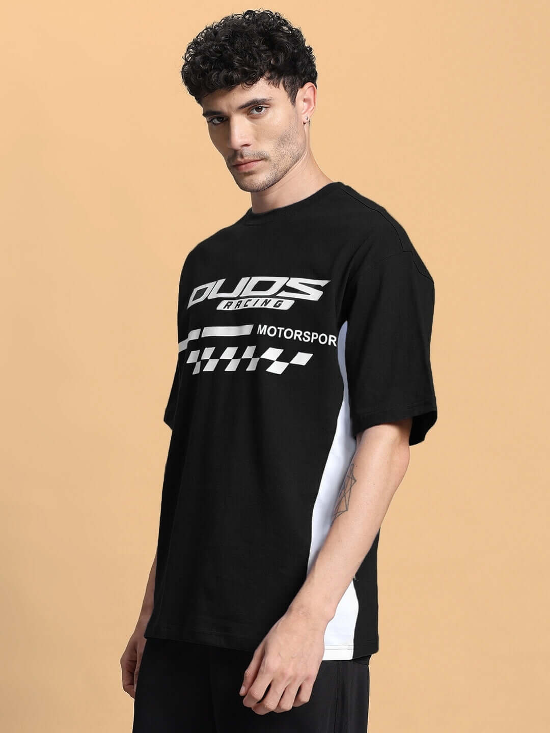 Man wearing INDY OVER-SIZED CLASSIC T-SHIRT BLACK with a sporty design on a beige background.