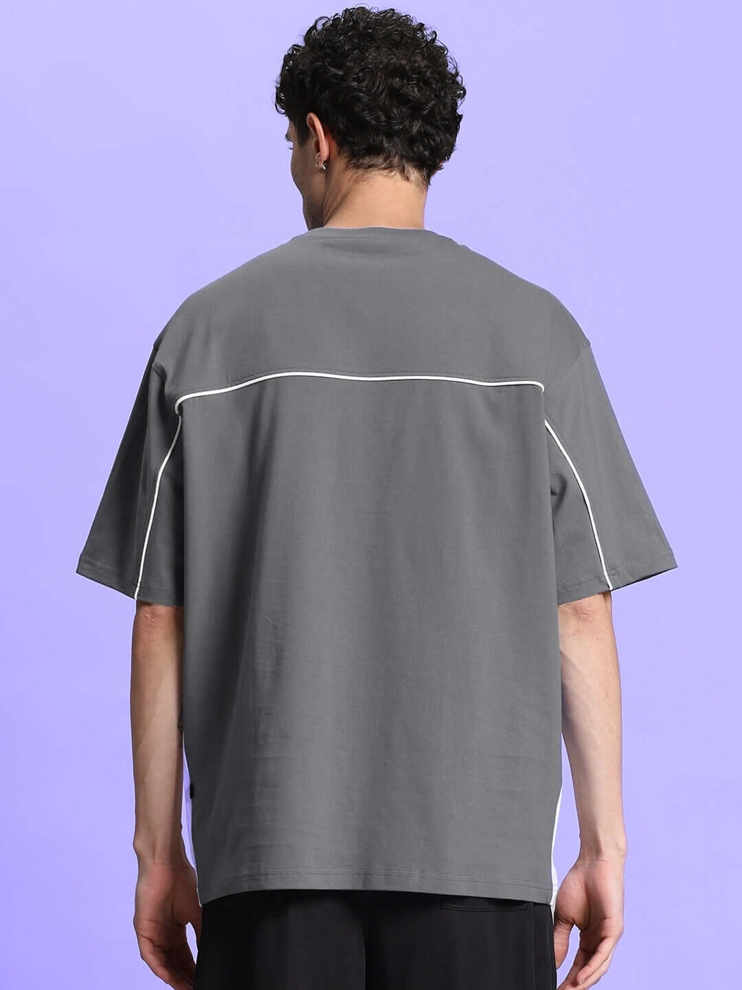 Back view of model wearing INDY OVER-SIZED CLASSIC T-SHIRT GREY on a purple background.