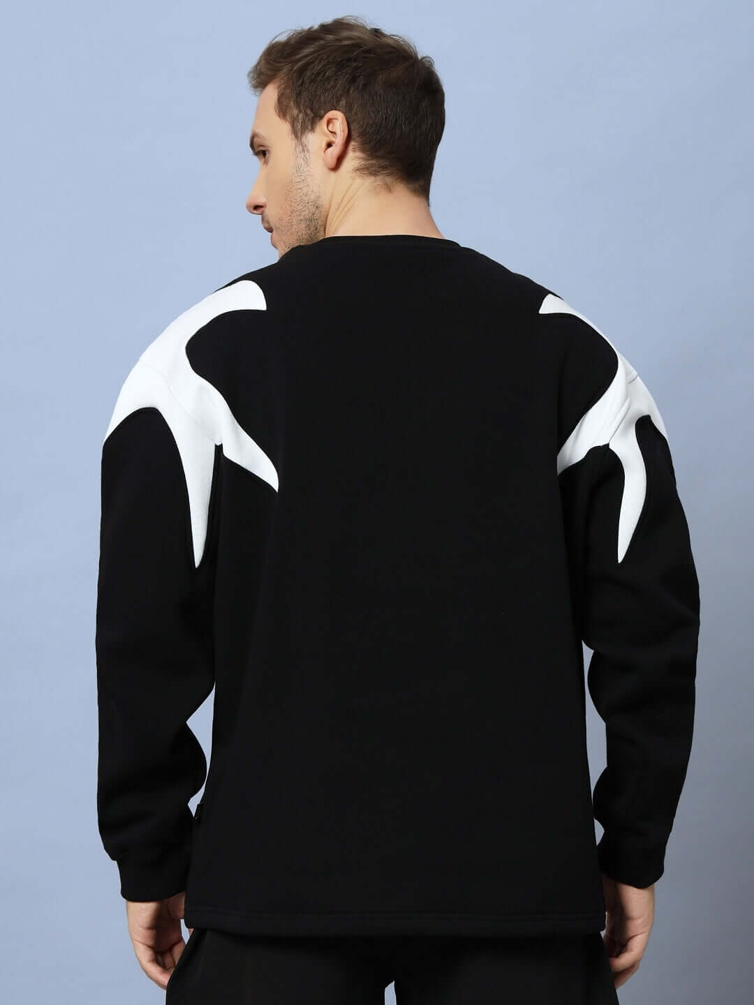 Back view of a model wearing the INFINITY SAGA OVERSIZED FLEECE SWEATSHIRT BLACK with white shoulder details.