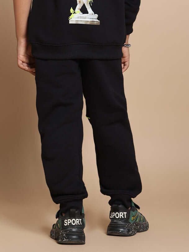 Child wearing black Innocent jogger pants for boys and girls, paired with sporty shoes, rear view on a neutral background.