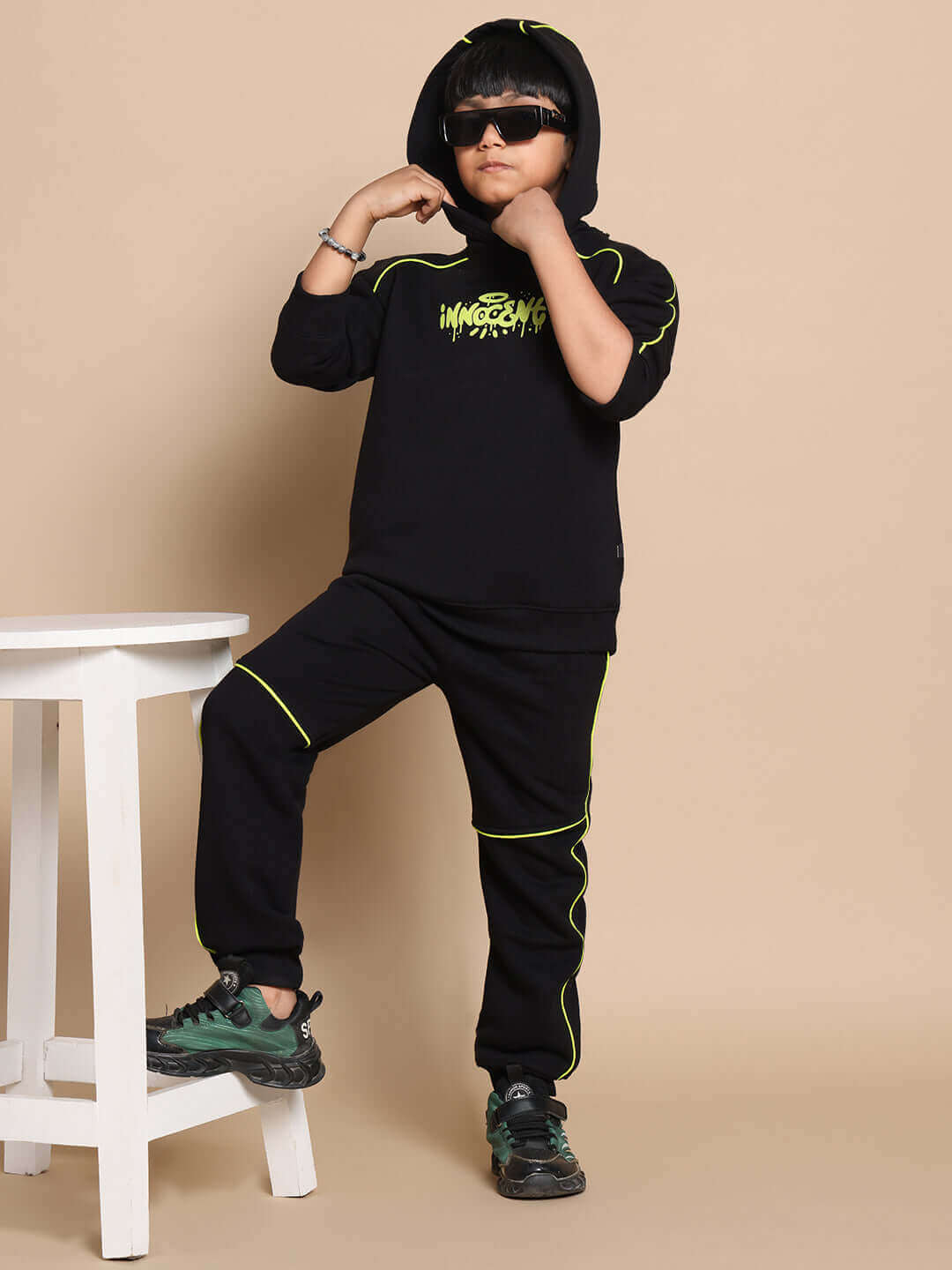 Child wearing Innocent Oversized Hoodie in black with neon accents, styled with matching pants and sneakers, showcasing trendy streetwear.