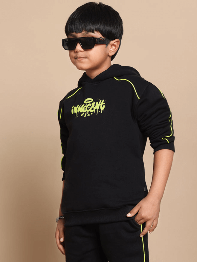 Boy wearing an Innocent oversized black hoodie with neon details, posing with sunglasses. Ideal for boys and girls. Trendy fashion statement.
