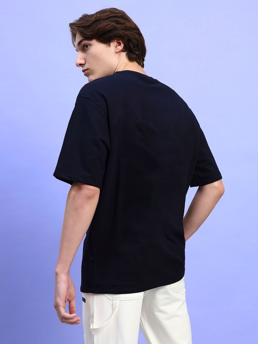 Rear view of model wearing INOSUKE PRINT OVERSIZED T-SHIRT BLACK in casual style against a light blue background.