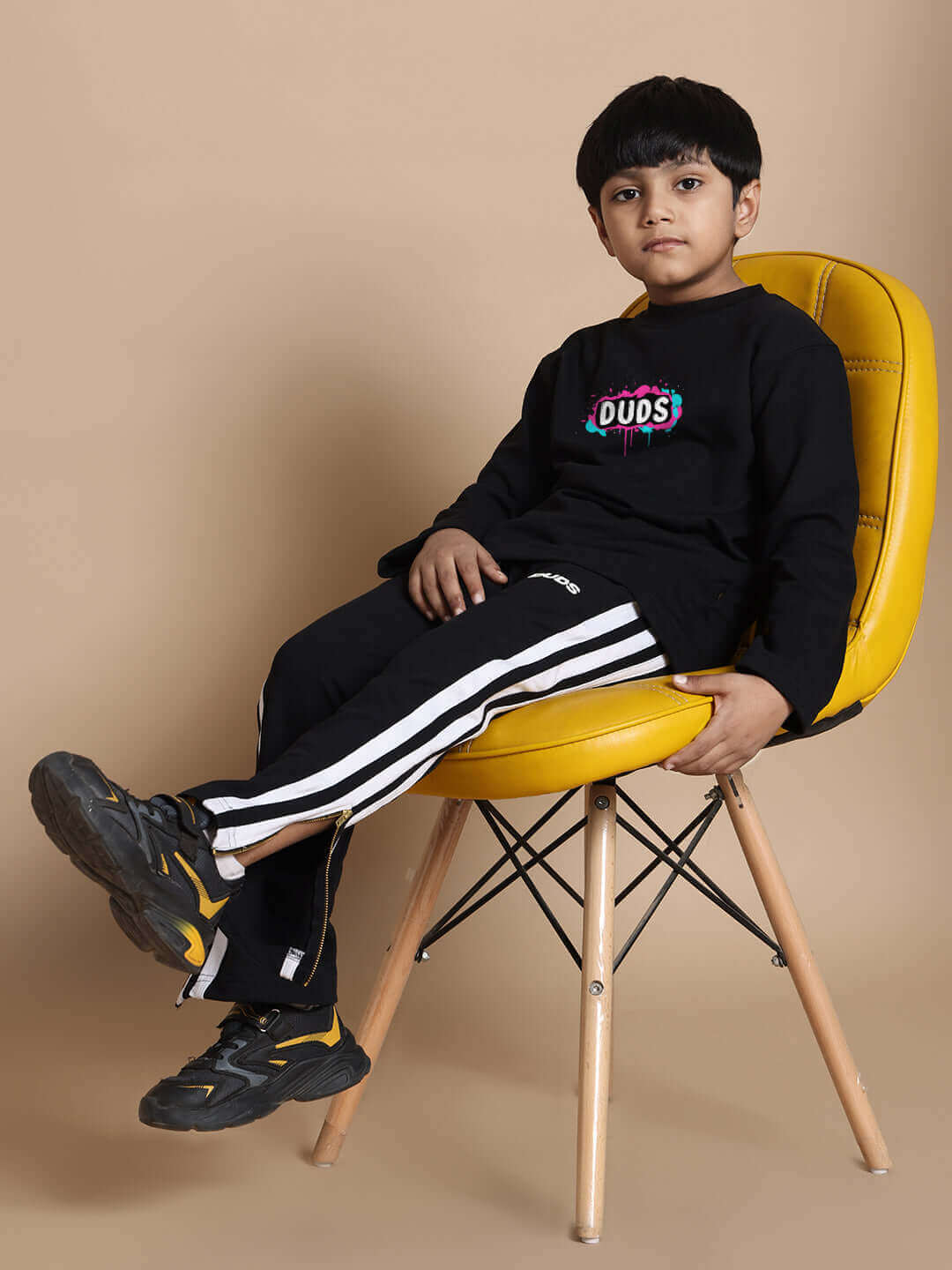 Child wearing INSANE RABBIT black co-ord set with joggers and logo top, seated on yellow chair; unisex, relaxed fit, premium cotton blend.