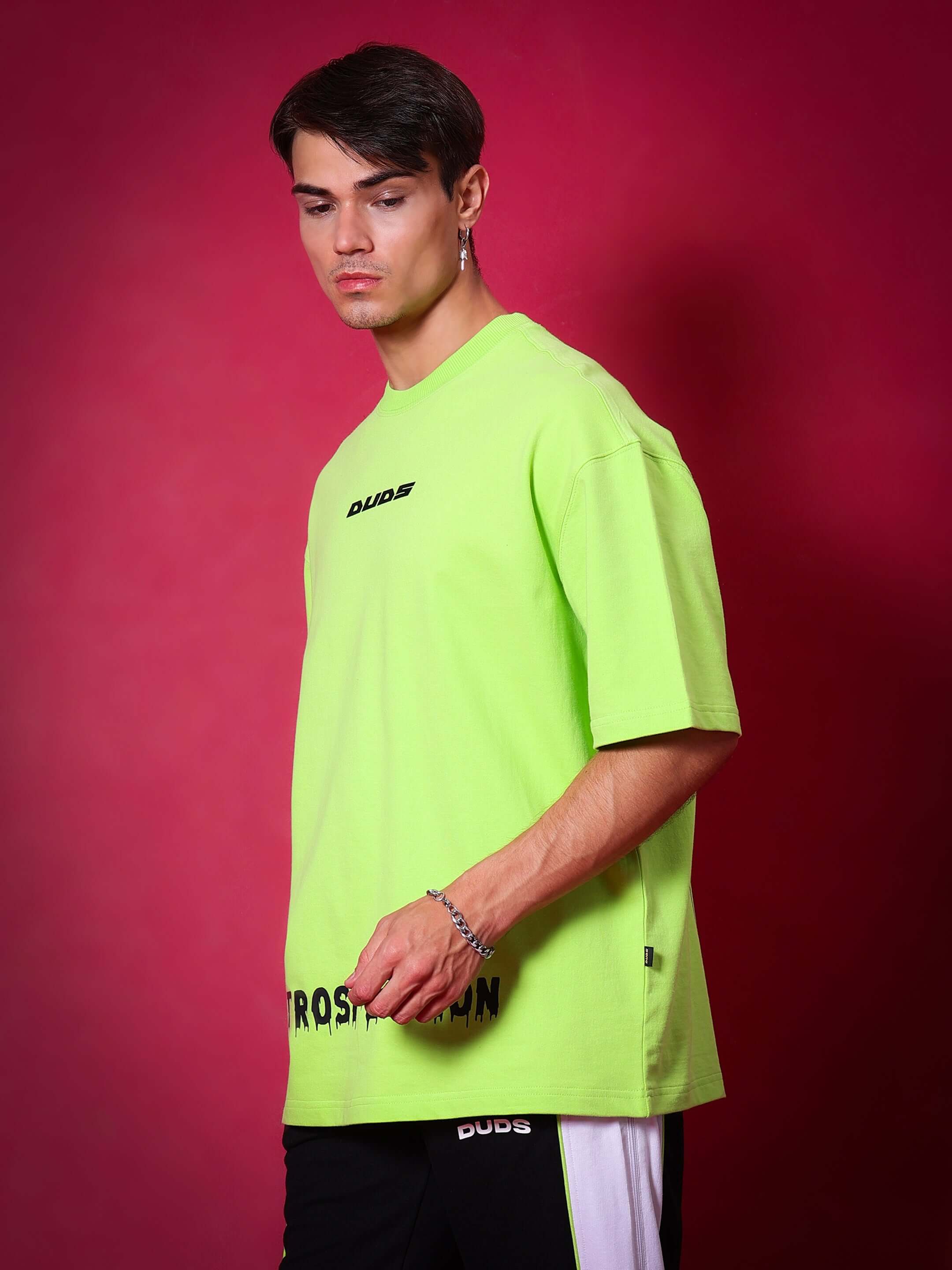 Model wearing INTROSPECTION oversized neon green t-shirt, premium cotton blend with French terry, styled against a red background.