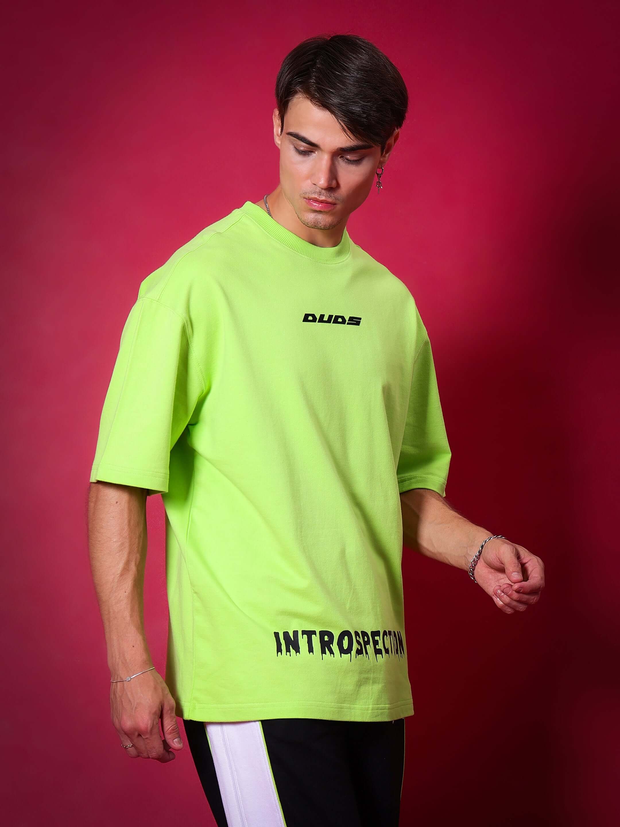 Model wearing neon green oversized INTROSPECTION T-shirt made of premium cotton and elastane, featuring bold lettering.