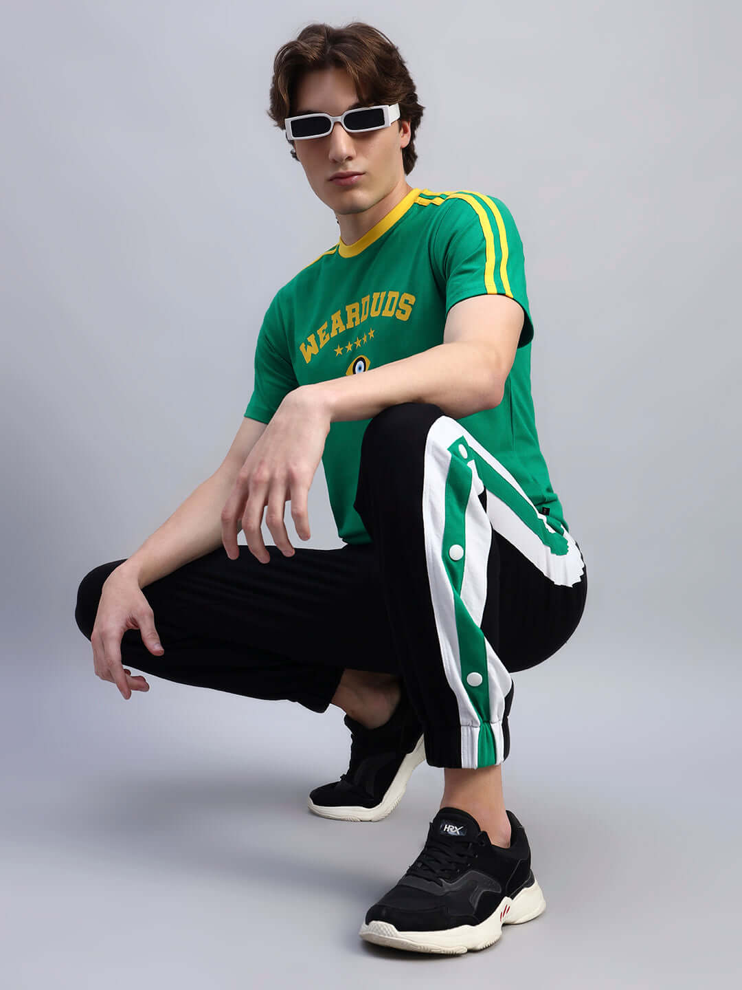Man wearing Irish Regular Fit Green T-shirt with striped pants and sunglasses, crouching in a studio setting.