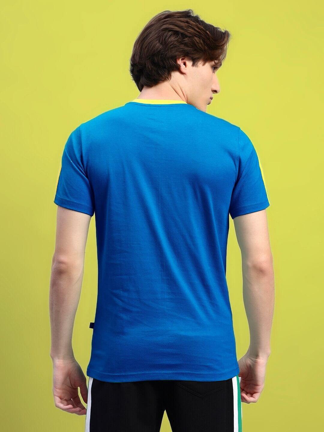 Back view of man wearing blue Irish regular fit T-shirt made from 100% cotton, showcasing casual style against green background.