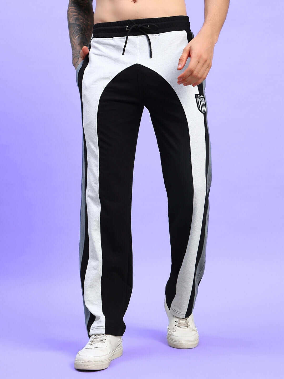 Man wearing Jamison color block relaxed-fit joggers in black melange-grey, standing against purple background. Made-to-order with custom fit option.