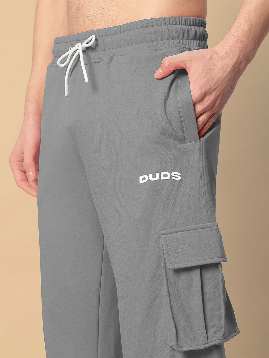 Close-up of grey relaxed fit joggers with pockets, featuring DUDS logo and adjustable waist tie.