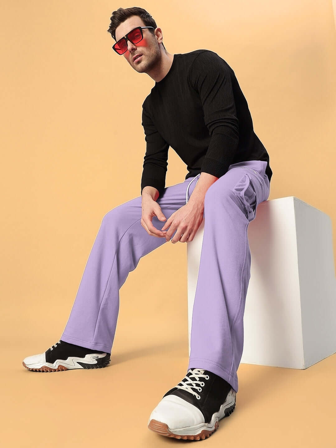 Model wearing JESS 5 Pocket Relaxed Fit Joggers in Lavender, styled with a black top and sneakers, sitting casually on a white block.