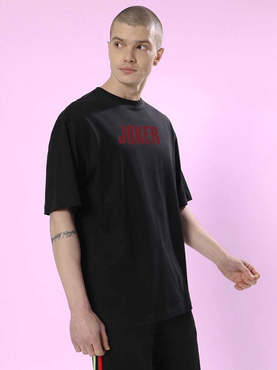 Model wearing JOKER PRINTED OVERSIZED T-SHIRT BLACK with red text on a pastel background.