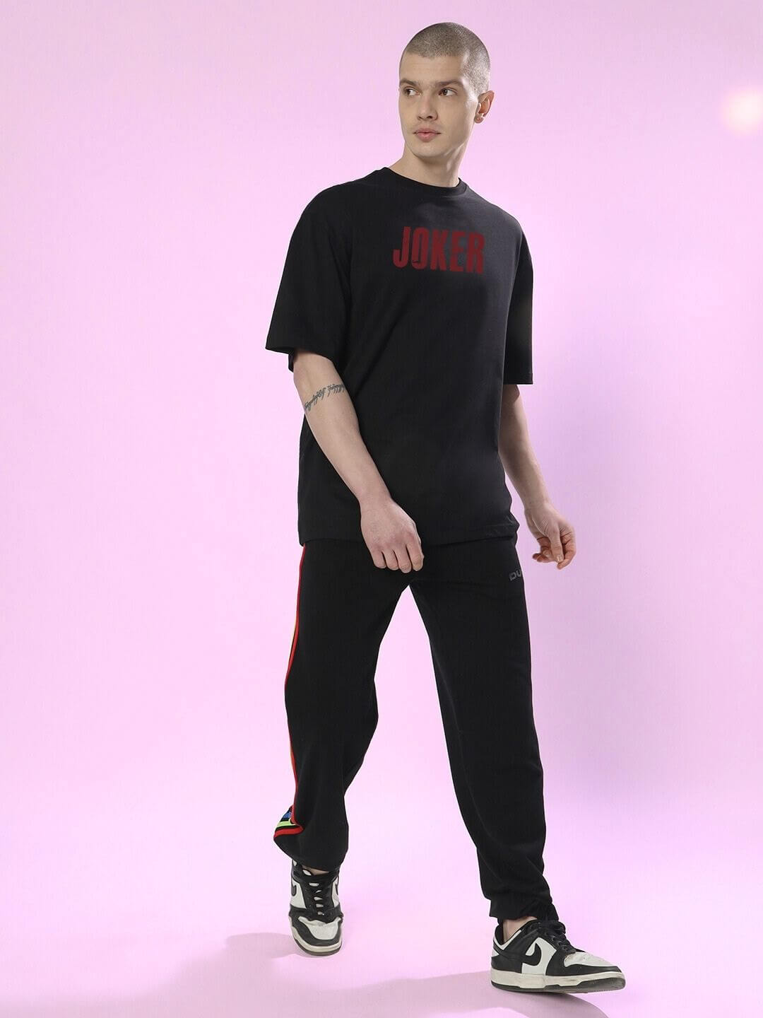 Man wearing JOKER PRINTED OVERSIZED T-SHIRT BLACK with streetwear style against pink background