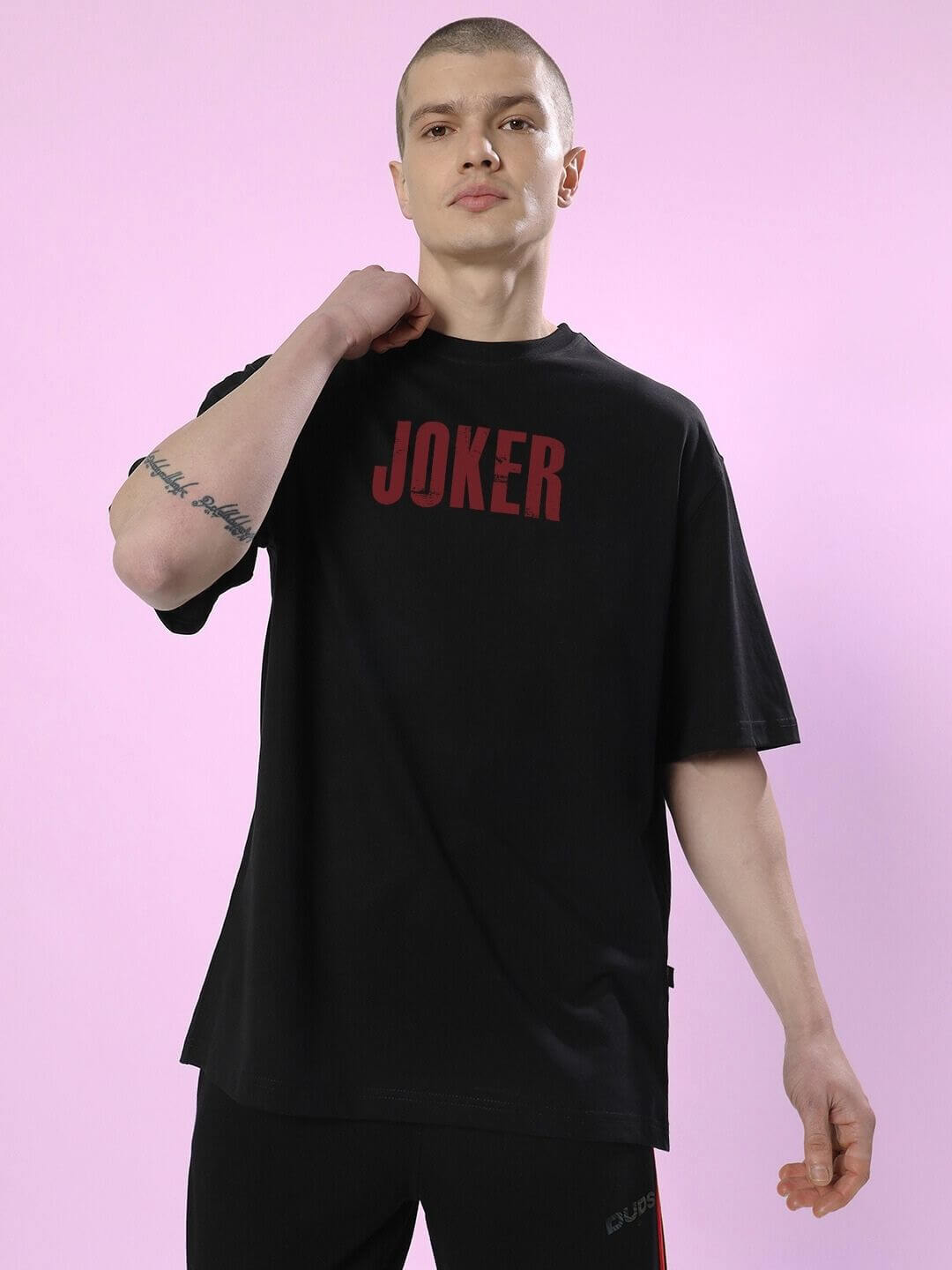 Model wearing JOKER PRINTED OVERSIZED T-SHIRT BLACK showcasing streetwear style against a pink background.