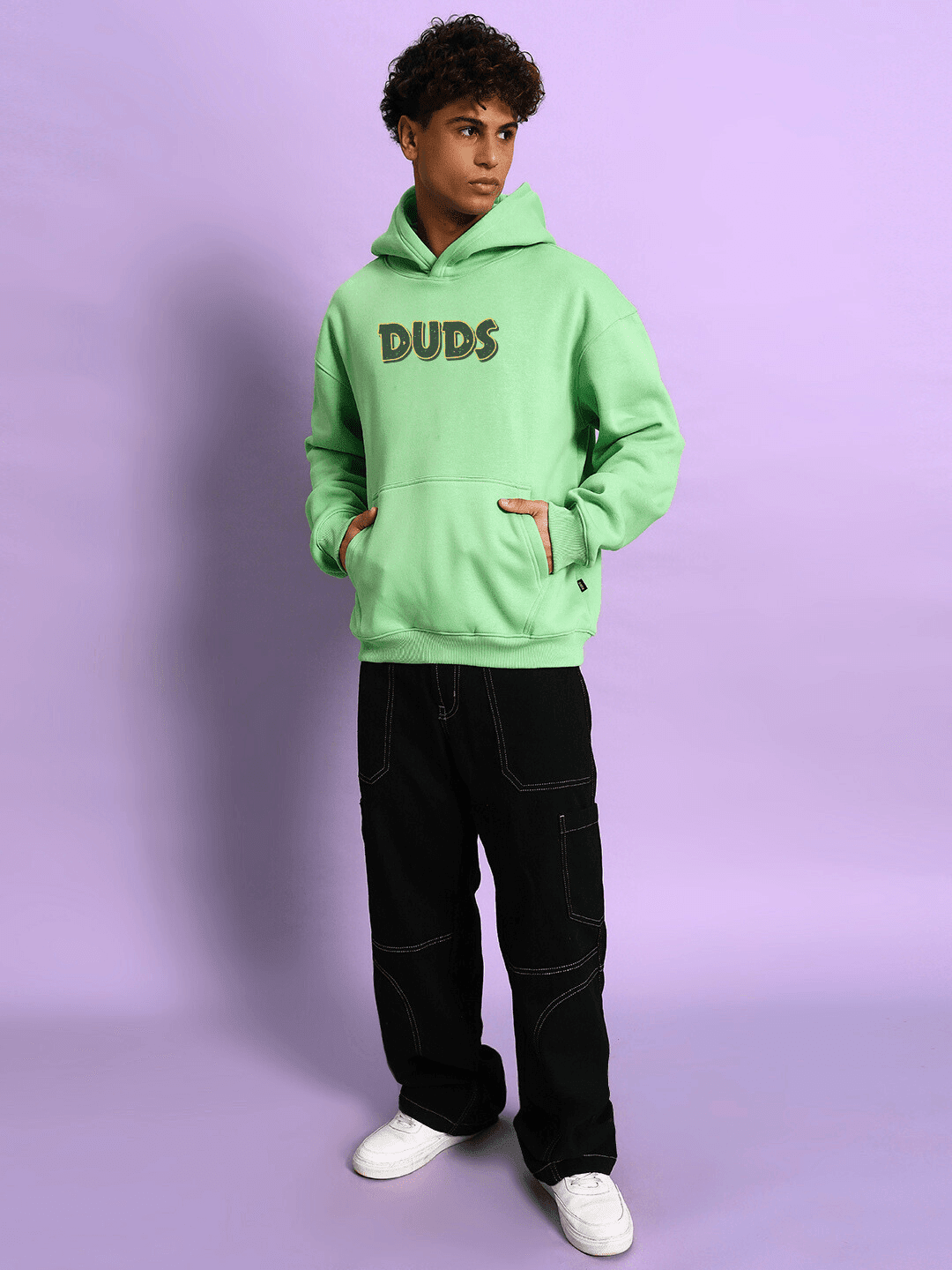 Person wearing JUDY NICK ZOOTOPIA FLEECE HOODIE GREEN with hands in pockets against purple background