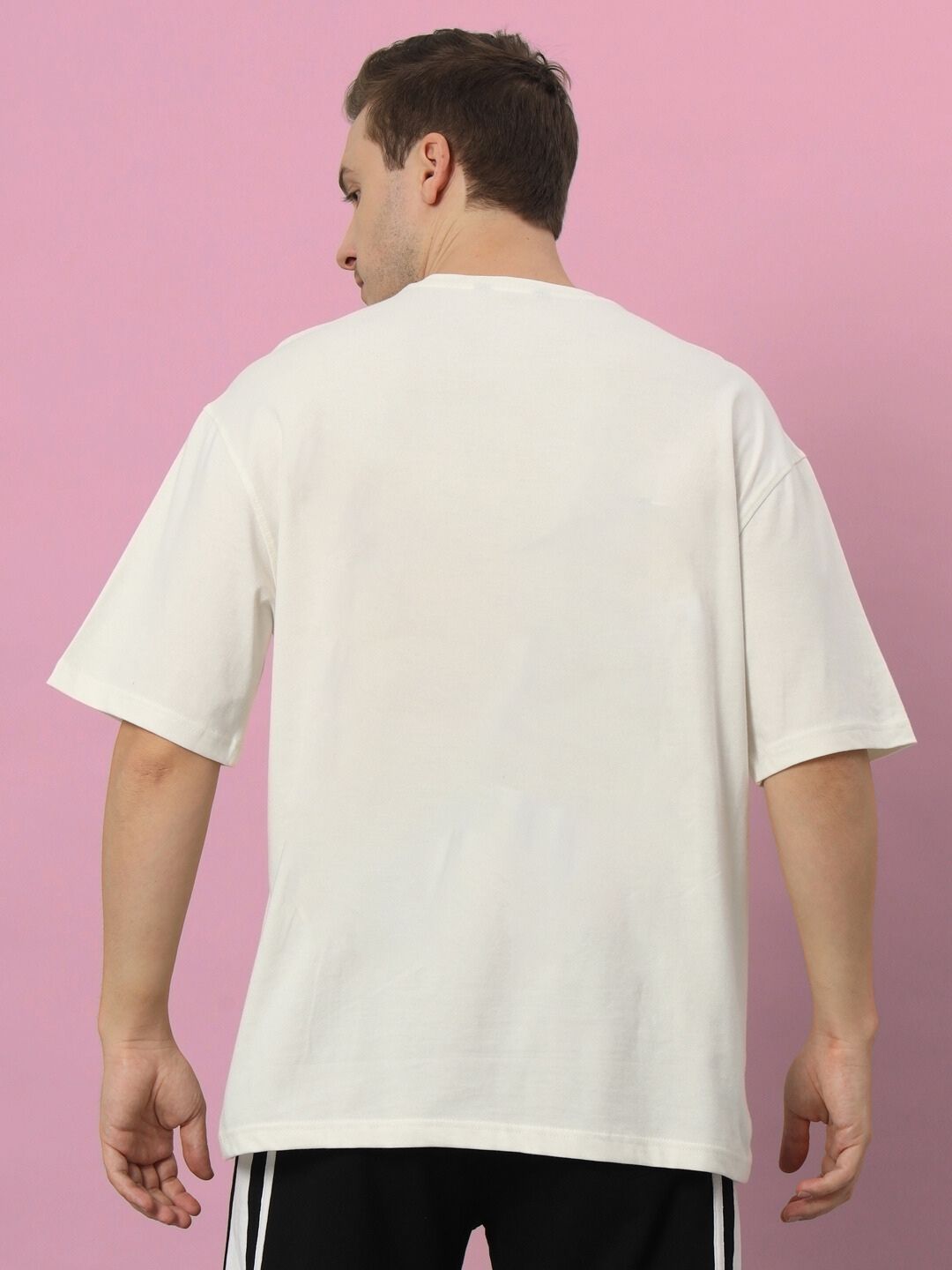 Back view of a KAKASHI PRINTED OVERSIZED T-SHIRT OFF-WHITE worn by a model, showcasing the fit against a pink background.