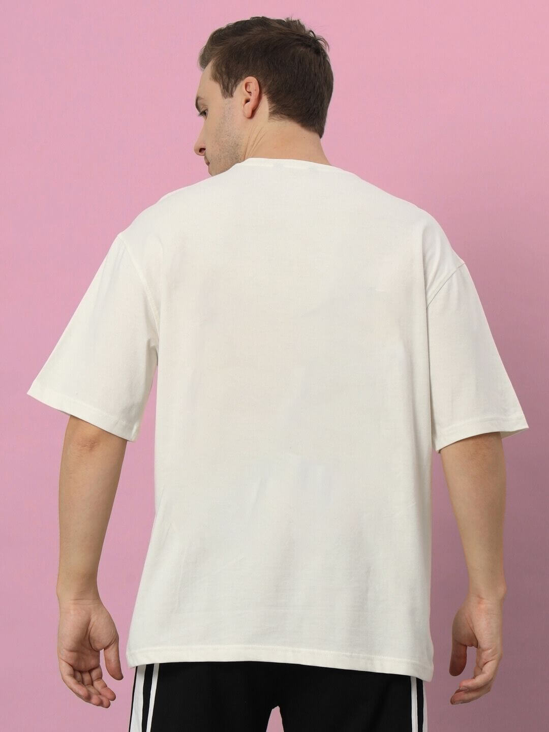 Model wearing KAKASHI PRINTED OVERSIZED T-SHIRT OFF-WHITE from the back, set against a pink background.