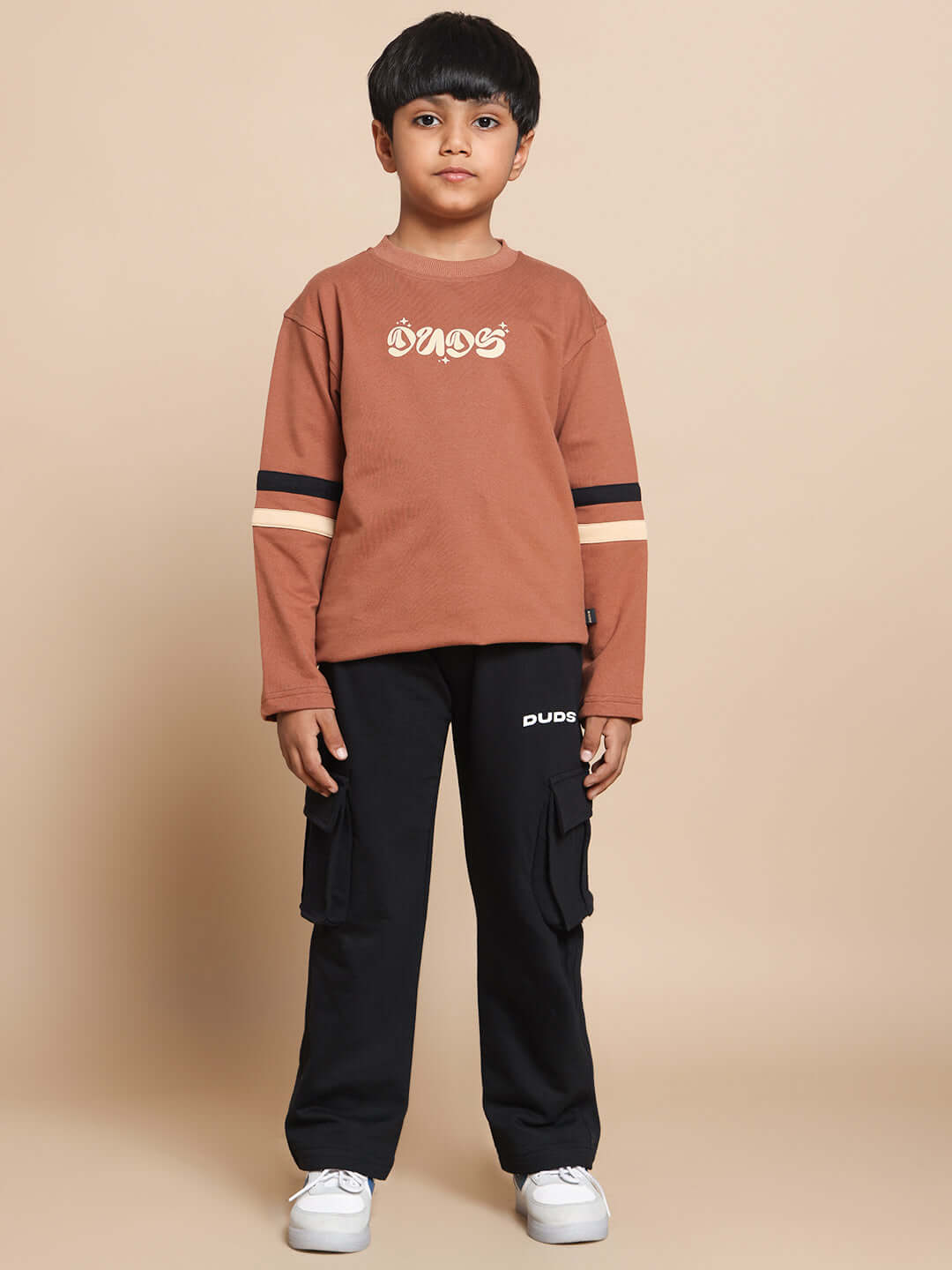 Child wearing brown-black KEEP FLYING co-ord set by DUDS, featuring brown long-sleeve top and black cargo pants. Ideal for boys and girls.
