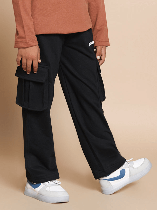 Child wearing black KEEP FLYING joggers with cargo pockets, designed by DUDS, paired with white sneakers.