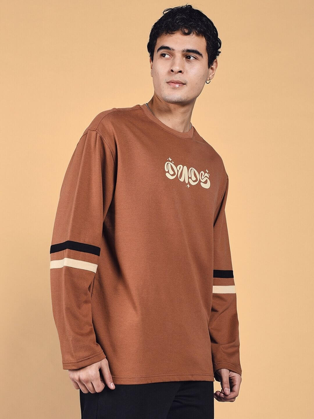 Model wearing a brown Keep Flying oversized sweatshirt with striped sleeves, designed with premium cotton fabric. Made in India.