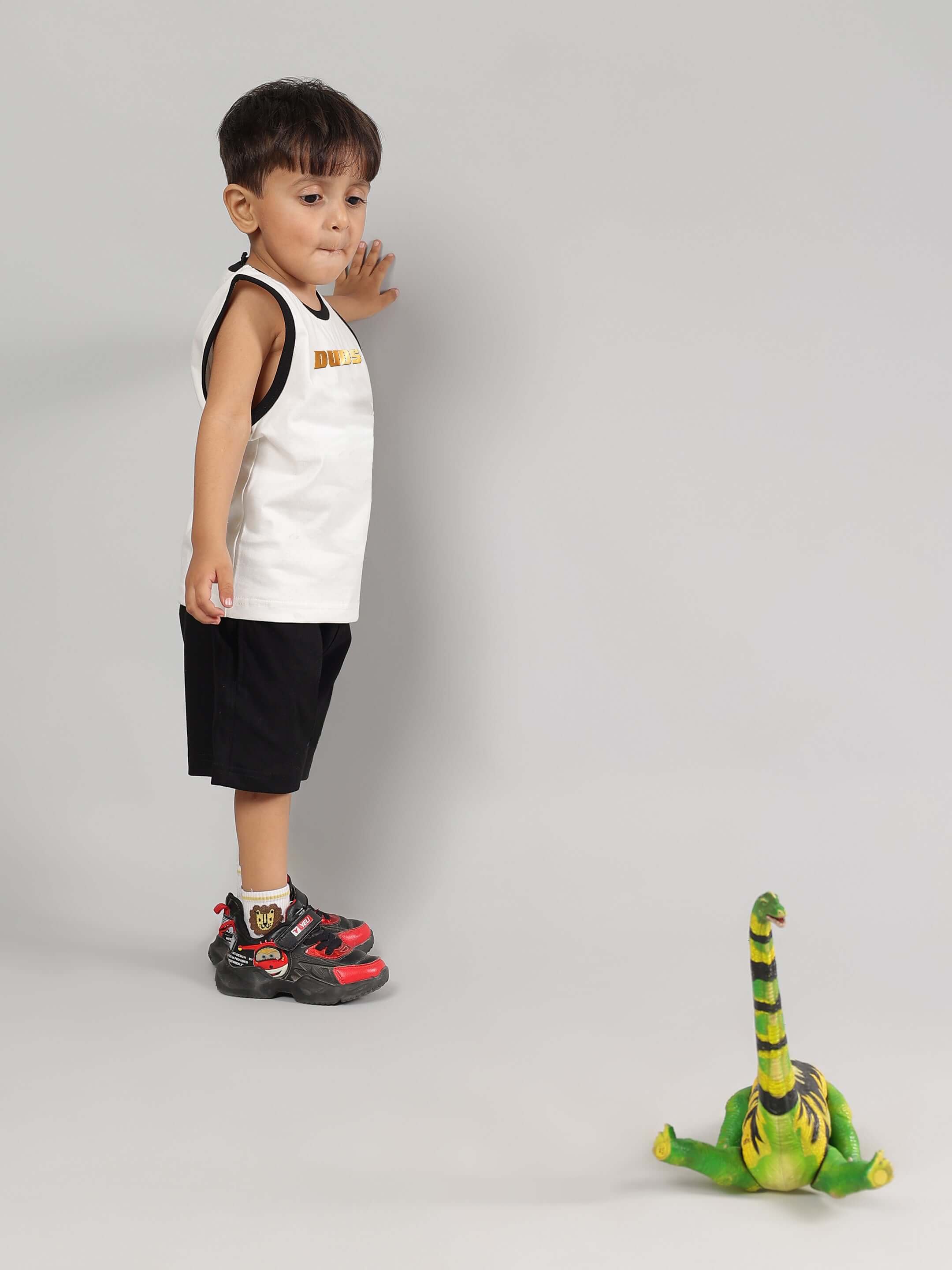 Young child wearing KEVIN Summer Co-ord in off white and black by DUDS, standing with a toy dinosaur.
