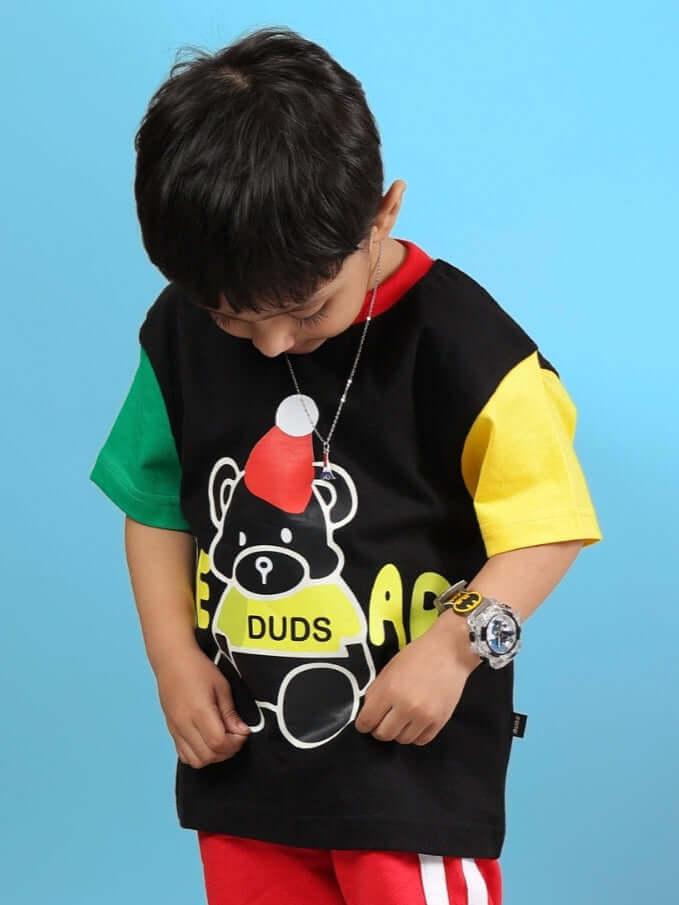 Child wearing a colorful bear graphic t-shirt with red, green, and yellow sleeves, against a blue background, looking down.