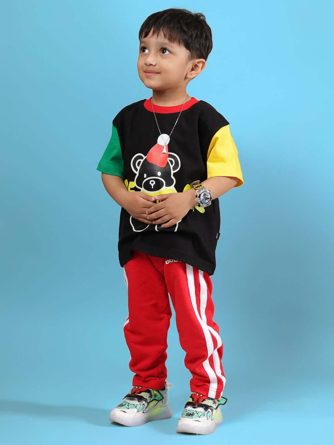 Child wearing a colorful t-shirt and red pants standing against a blue background