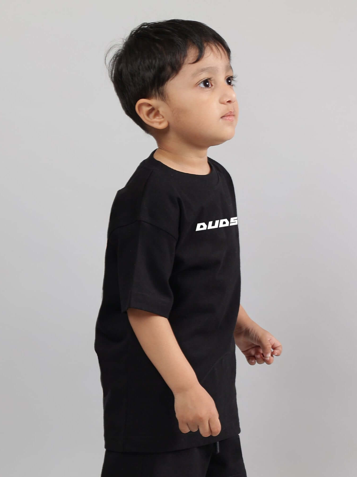 Child wearing black 'Enjoy the Wind' t-shirt by DUDS, tailored for boys and girls, featuring a comfortable fit.