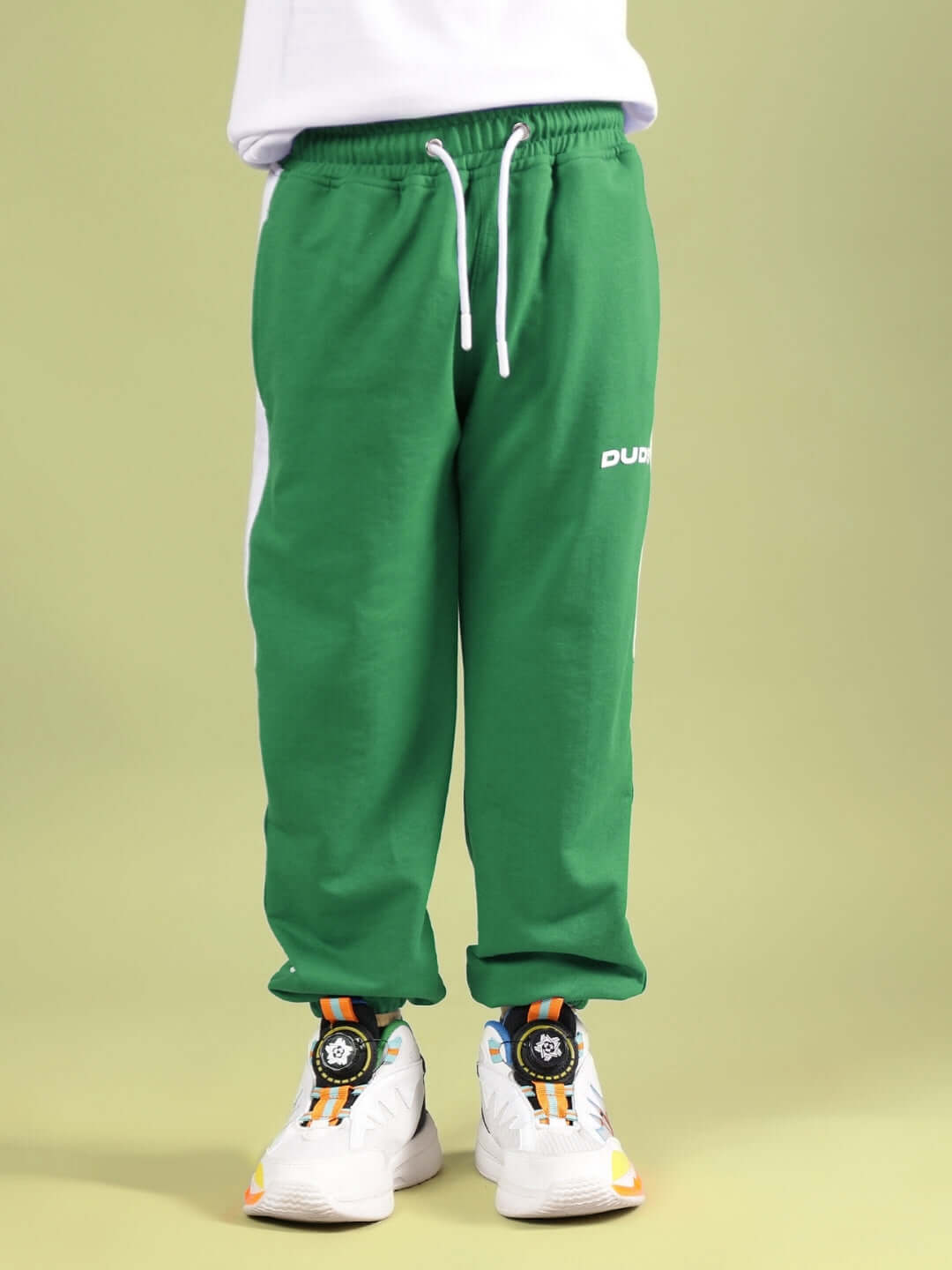 Green sweatpants with white accents styled with white sneakers on a child model.