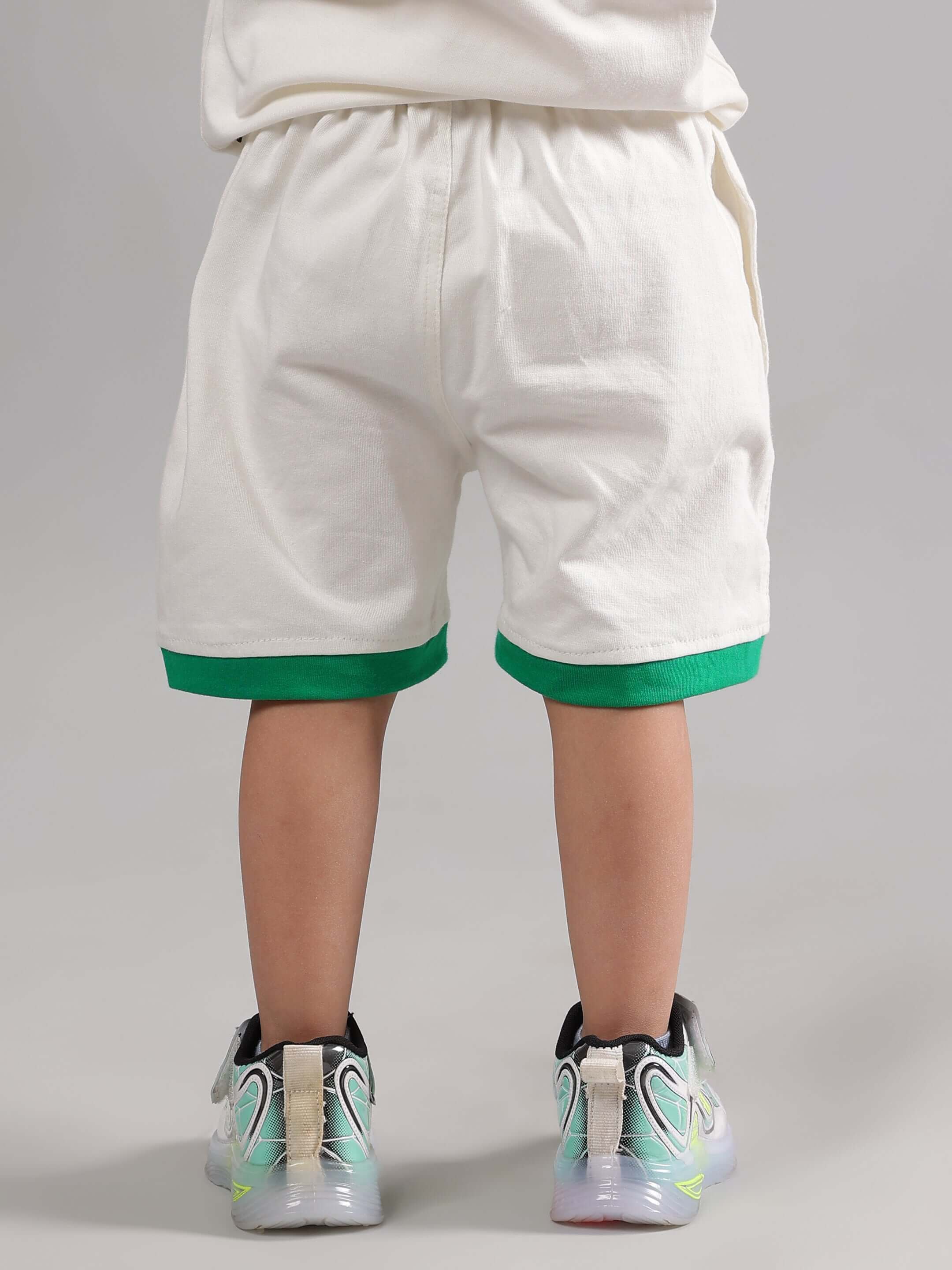 Child wearing SLOTH CO-ORD FOR BOYS GIRLS OFF WHITE with green-trimmed shorts and sneakers, back view.