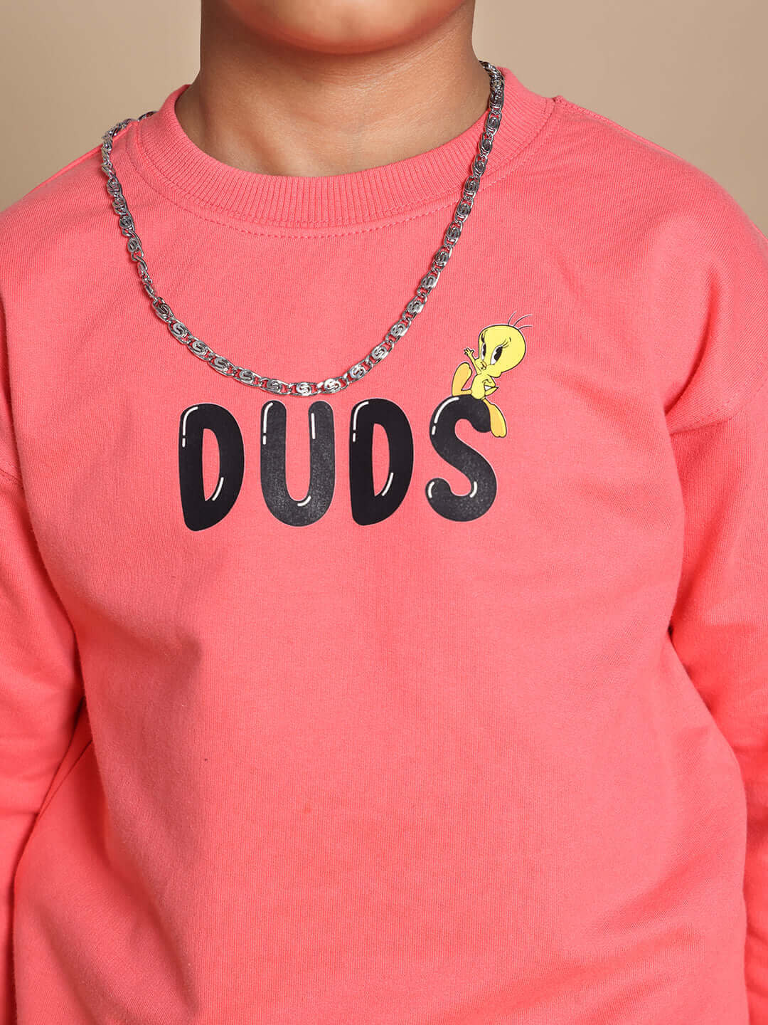 Child wearing peach DUDS sweatshirt with cartoon detail, highlighting comfortable and stylish fashion for kids.