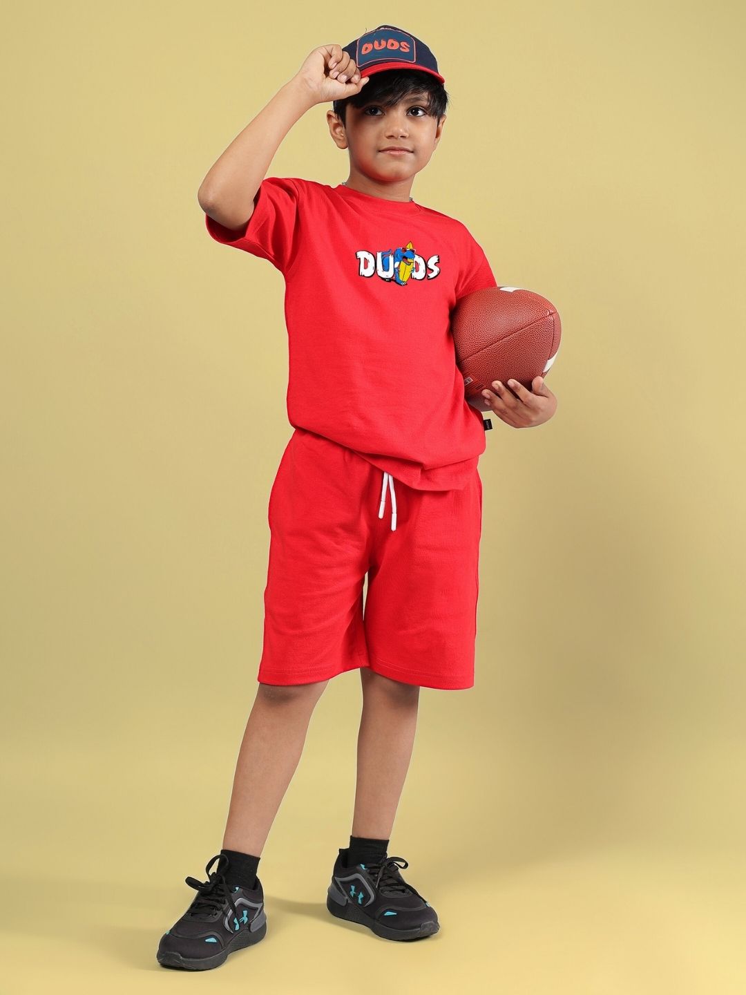 CATCH THE WAVES CO-ORD FOR BOYS & GIRLS RED outfit featuring a child holding a football, wearing a cap, on a yellow background.