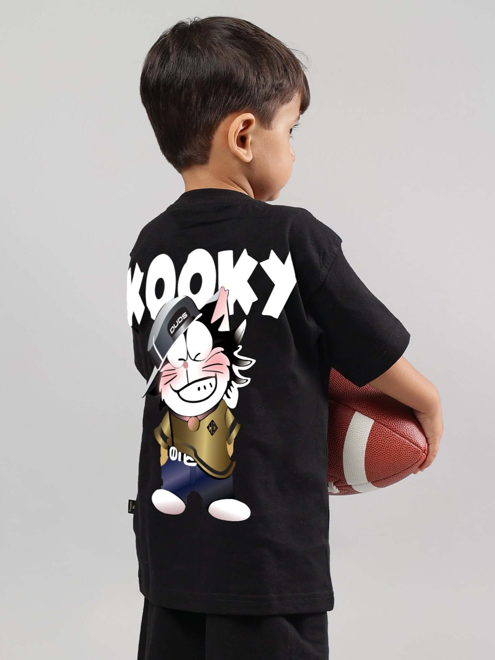 Child wearing KOOKY black t-shirt holding a football, showcasing playful cartoon design for boys and girls.