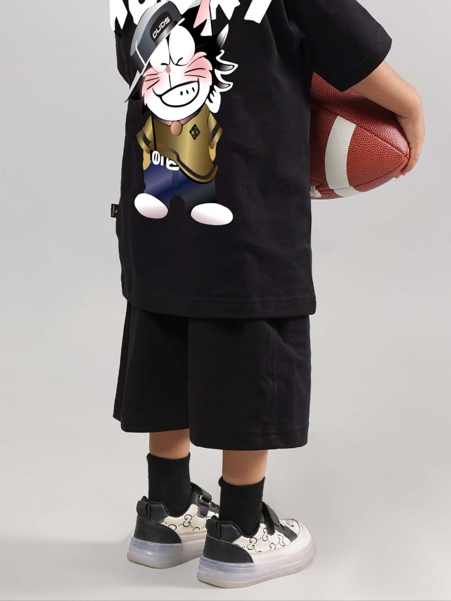 Child wearing Kooky black shorts holding a football, showcasing custom-fit options for boys and girls, made to order by DUDS.