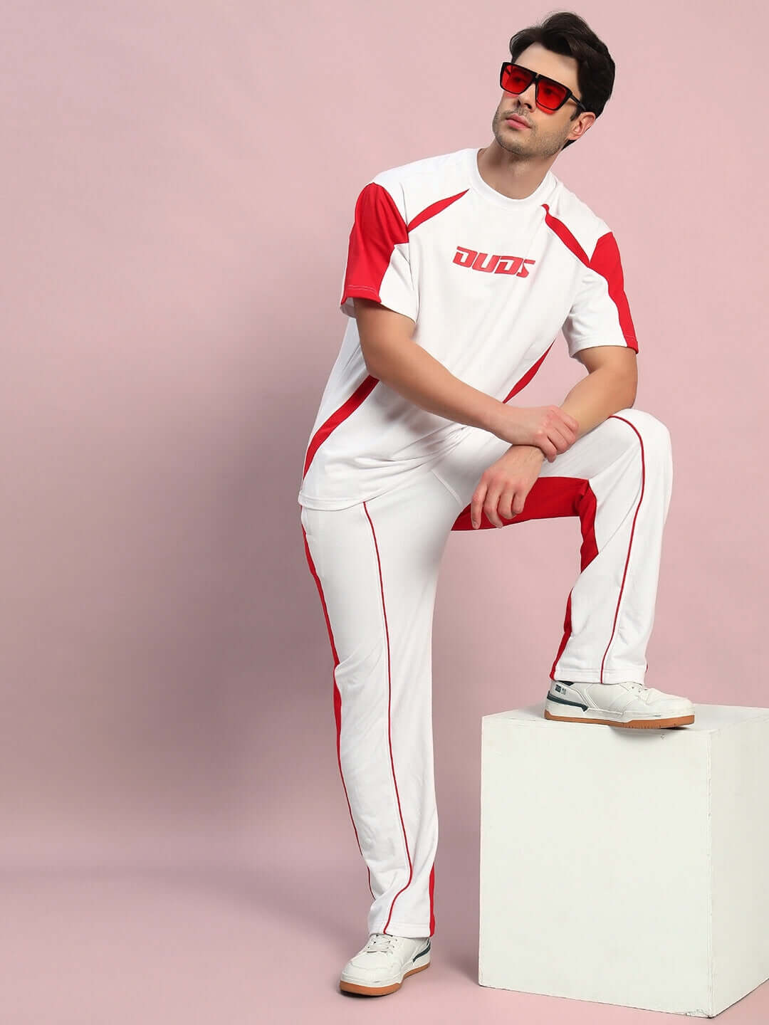 Model wearing Lagoon Relaxed Fit Joggers in white and red by DUDS, standing confidently with hands in pockets on a pink background.