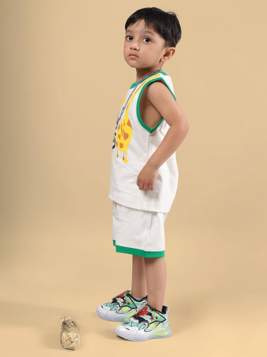 Child wearing LET'S SMILE CO-ORD FOR BOYS AND GIRLS OFF WHITE set, featuring giraffe print, standing sideways with casual shoes.