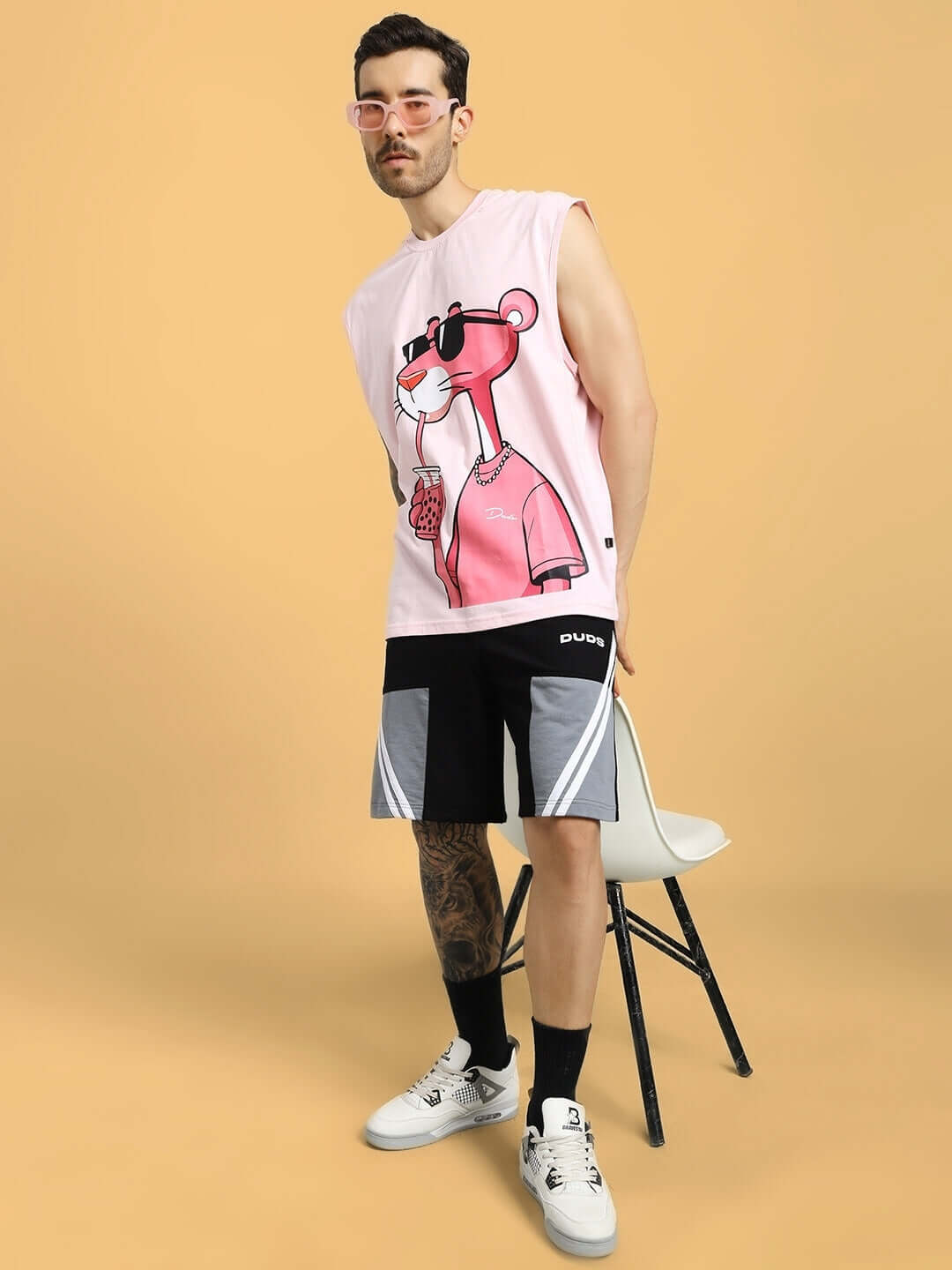 Model wearing LEWIN CHINO REGULAR FIT SHORTS BLACK-GREY with a stylish pink graphic shirt, standing against a beige background.