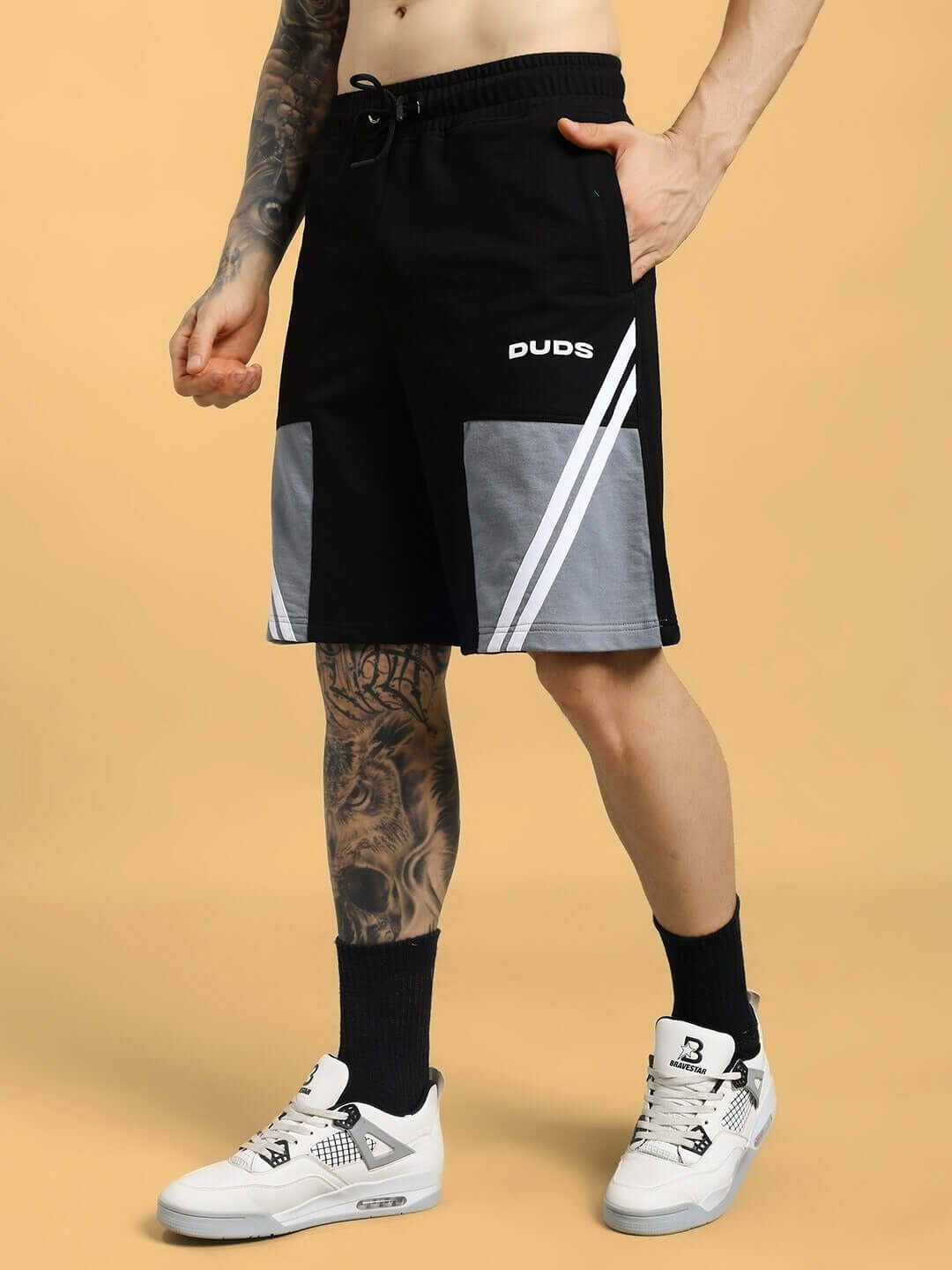 Man wearing LEWIN CHINO REGULAR FIT SHORTS BLACK-GREY with sneakers on tan background