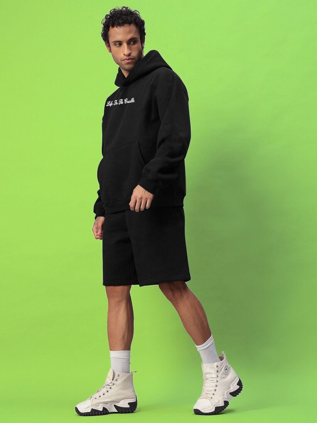 Model wearing LIFE IN THE CRUCIBLE PRINTED FLEECE CO-ORD BLACK against green background, showcasing urban style and comfort.
