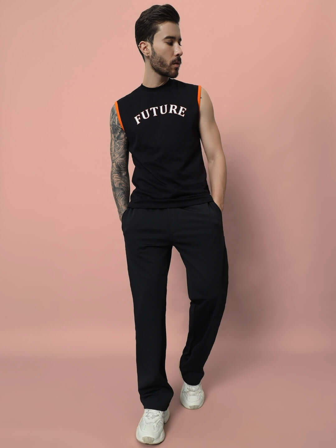 Man wearing black LIMBER RELAXED PANT JOGGER, black sleeveless shirt with 'FUTURE' text, standing against coral background.