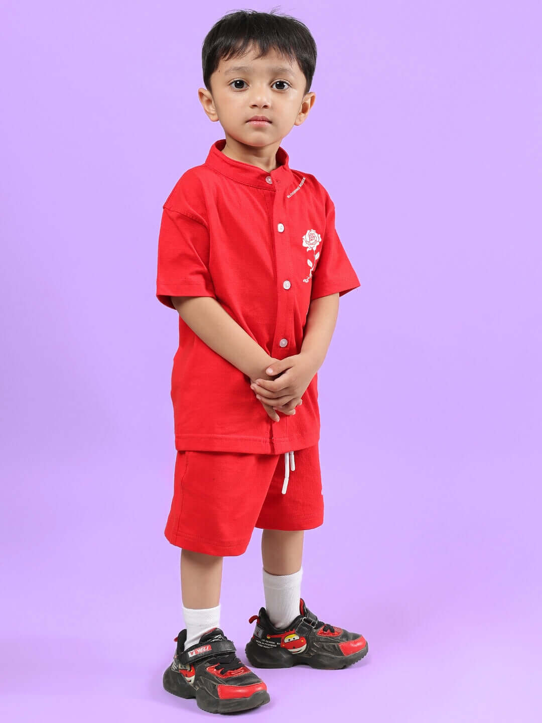 A child wearing a LIMBO CO-ORD FOR BOYS & GIRLS RED set, featuring a red shirt and shorts, standing against a purple background.