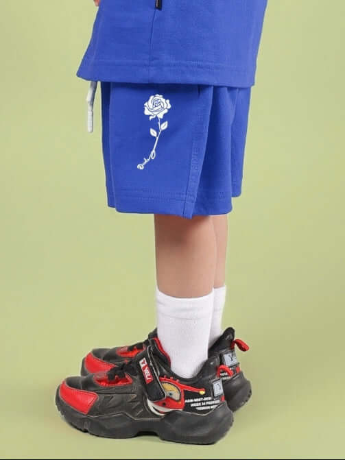 Child wearing LIMBO SHORTS FOR BOYS & GIRLS BLUE, featuring rose design, paired with chunky black and red sneakers.