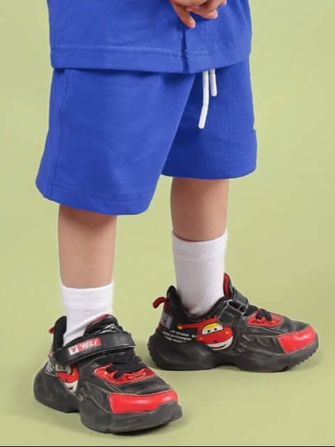 Child wearing LIMBO SHORTS FOR BOYS & GIRLS BLUE with sneakers on a green background, showcasing comfort and style for active kids.