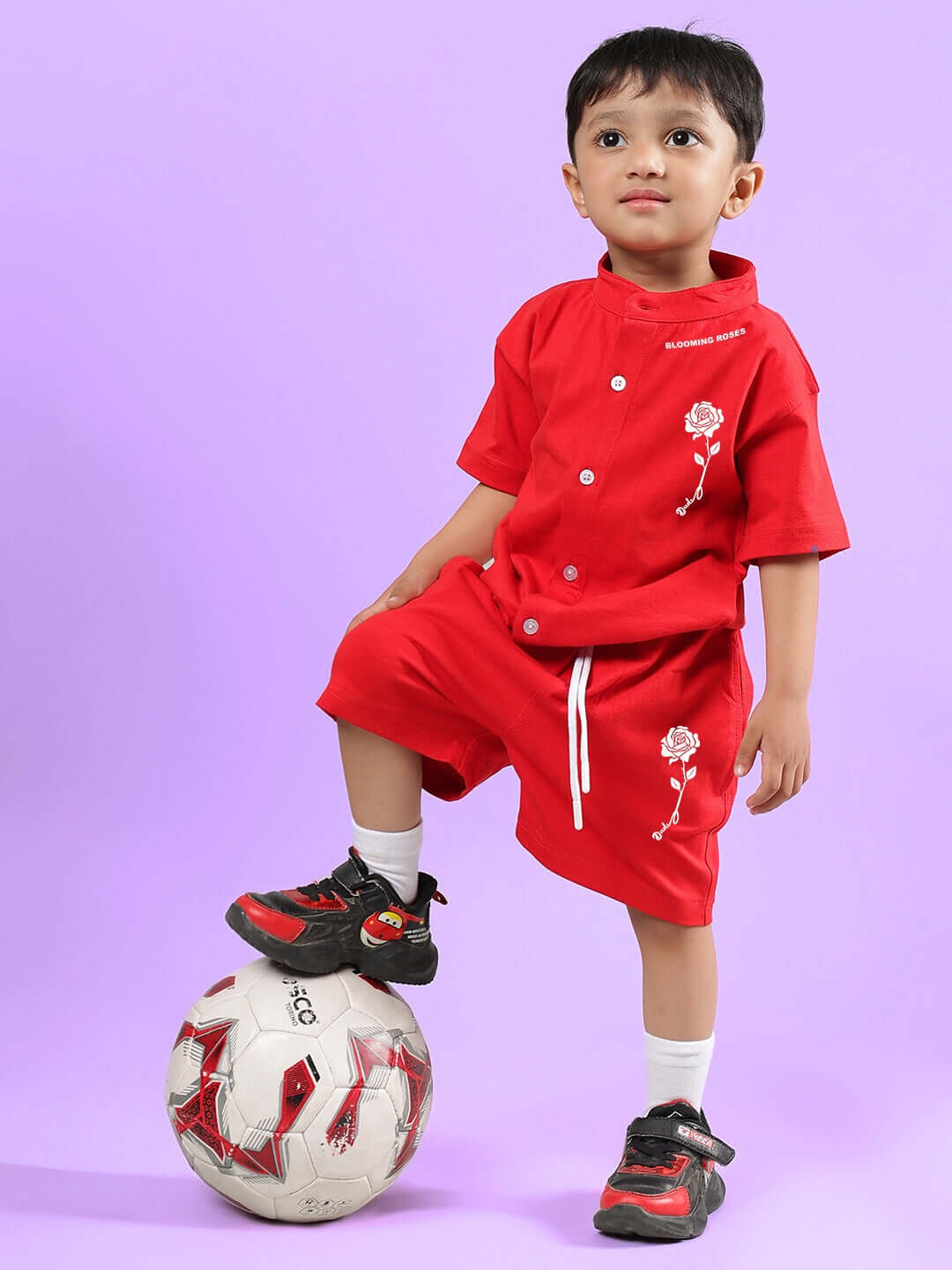 Child wearing LIMBO SHORTS FOR BOYS & GIRLS RED, posing with a soccer ball. Made to order. Custom fit available. Red shorts set against purple background.